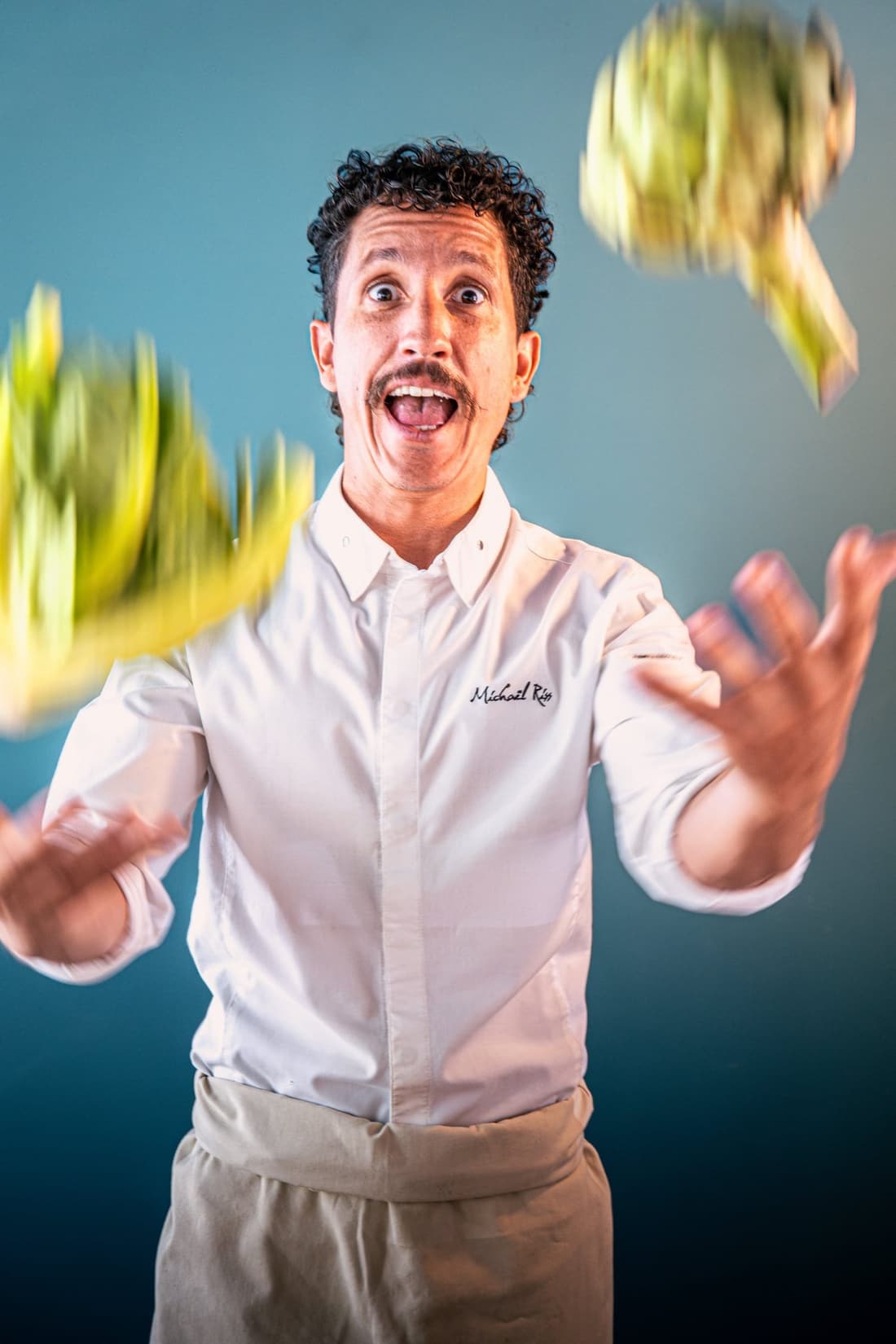 Portrait du chef Michaël Riss en veste blanche devant un mur bleu
