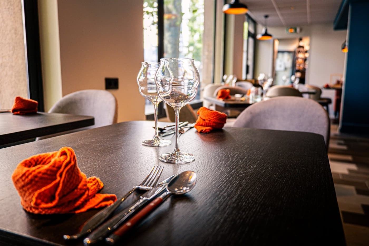 La salle du restaurant : tables dressées, verres à vin et bouteilles, serviettes rouges